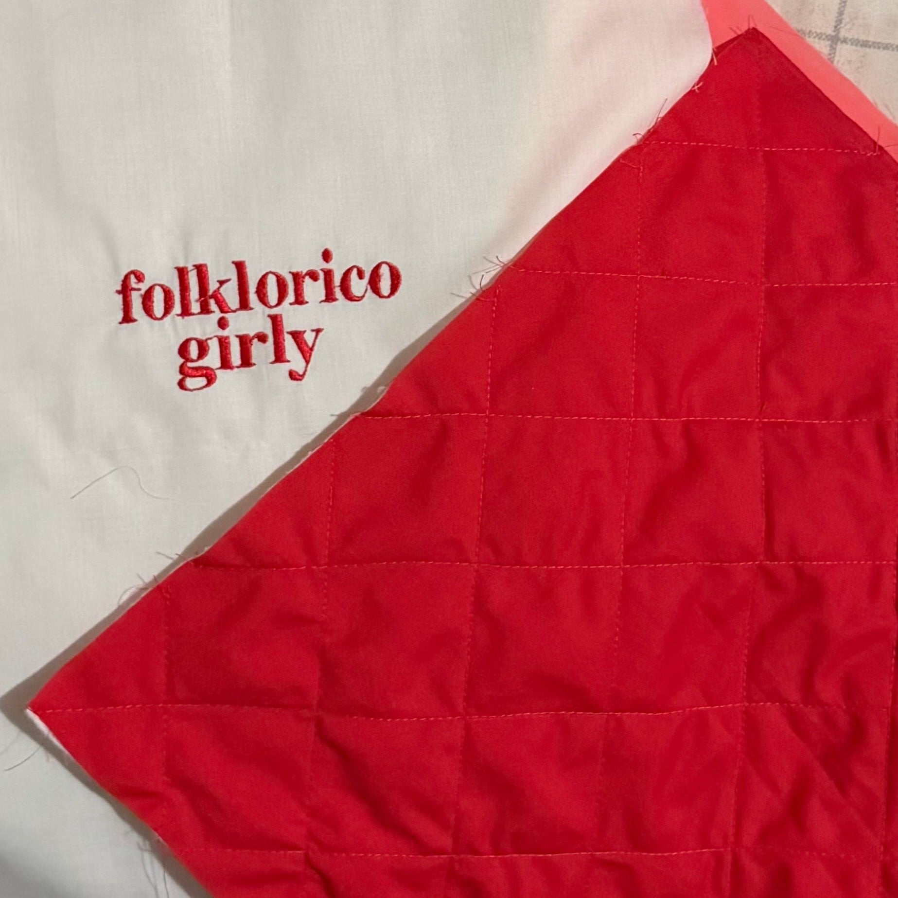 Red fabric quilt with 'folklorico girly' embroidered text on an white fabric