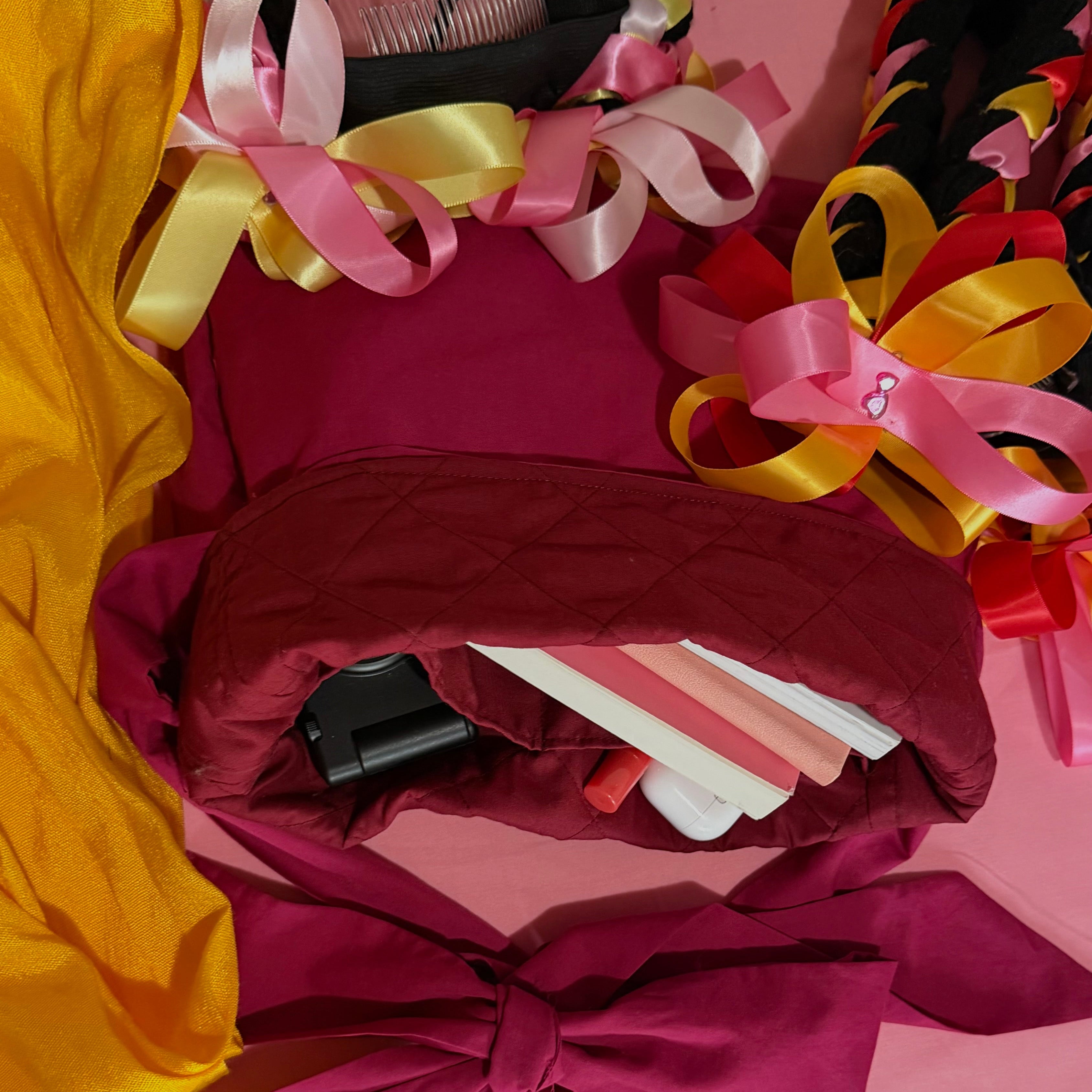 hair accessories with colorful ribbons laying on top of a quilted, magenta tote bag stuffed with books and other small items on a pink background