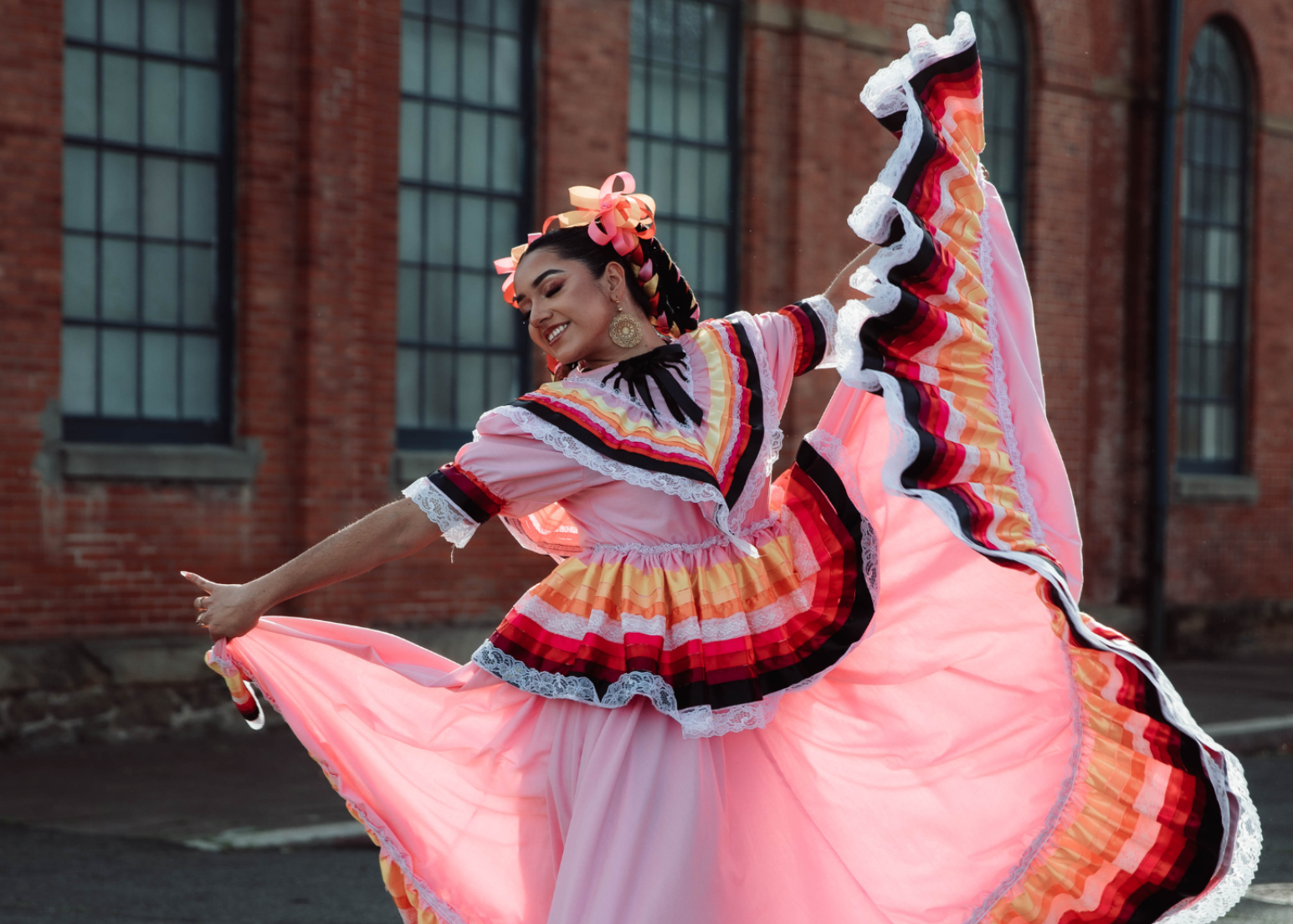 Dancer in a colorful traditional Mexican folklore outfit performing in front of a brick building.